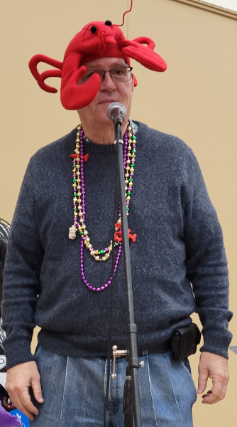A man standing at a microphone with a lobster hat and multicolored necklaces