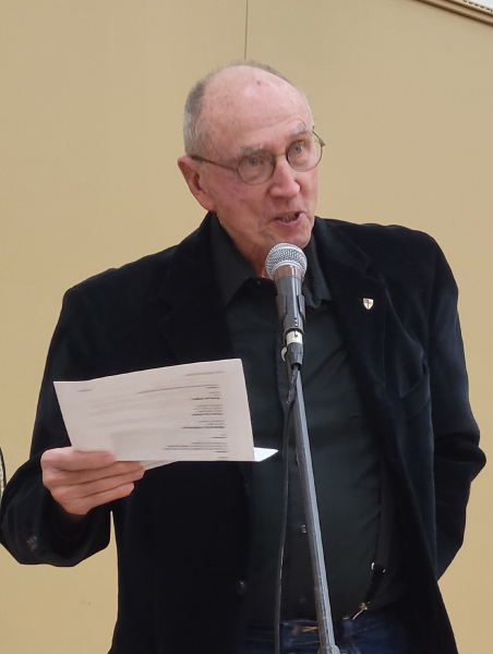 A man standing at a microphone reading a piece of paper being held