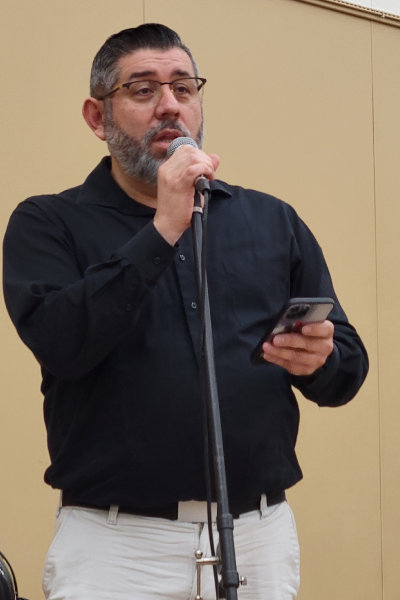 A man standing at a microphone reading from a phone