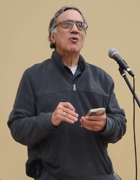 A man standing at a microphone reading from a phone