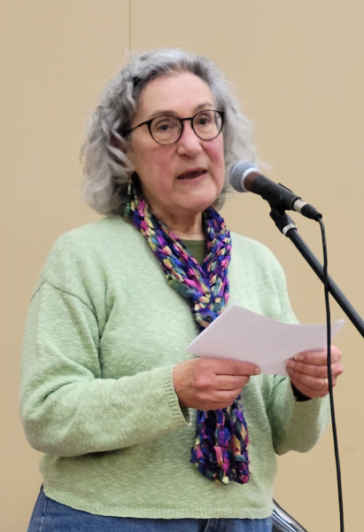 A woman standing at a microphone reading a piece of paper being held